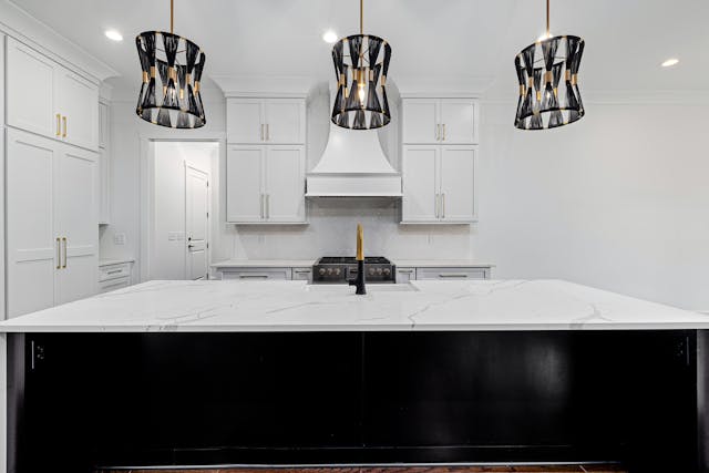 a-modern-kitchen-with-a-white-marble-island-three-pendant-lights-with-black-and-gold-shades-white-cabinets-and-a-stainless-steel-stove a-modern-kitchen-with-a-white-marble-island-three-pendant-lights-with-black-and-gold-shades-white-cabinets-and-a-stainless-steel-stove